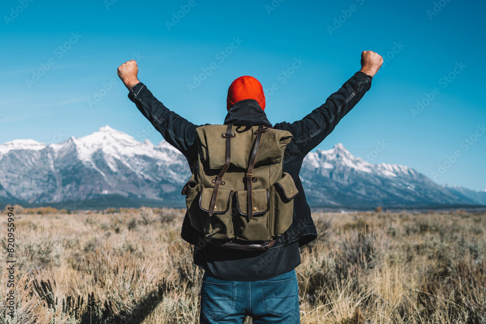 Back view of hipster guy standing with raising hands feeling excited with beautiful view of winter mountains ahead, male traveler wanderlust happy and celebrating achievement getting to destination Back view of hipster guy standing with raising hands feeling excited with beautiful view of winter mountains ahead, male traveler wanderlust happy and celebrating achievement getting to destination