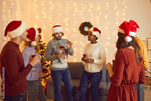 Diverse international friends with glasses of champagne make toast on New Year party at home. Multiracial people celebrate Christmas together in decorated beautiful house. Winter holiday concept.