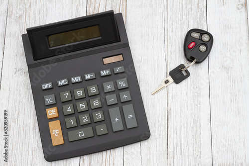 A black calculator with car keys on wood desk