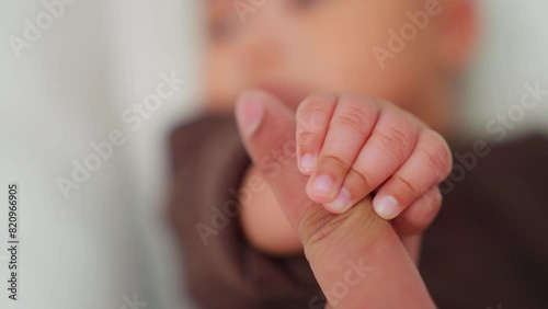 Newborn baby playing with mother's hand and finger lying on bed. baby little cute reaching touching mom finger. Baby holding parents finger. Parent holding newborns hand. mama takes care child.