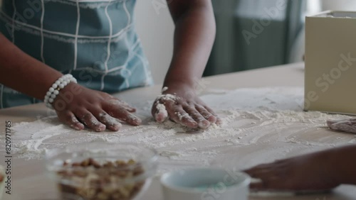 Close-up of hands of unrecognizable black woman and children dusting flour over kitchen table surface going to prepare dough-based dish or knead pastry for bread