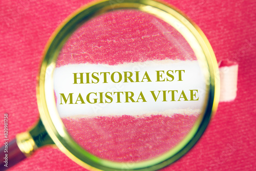 Historia est vitae magistra (History is the tutor of life) Latin phrase through a magnifying glass under a piece of torn paper photo