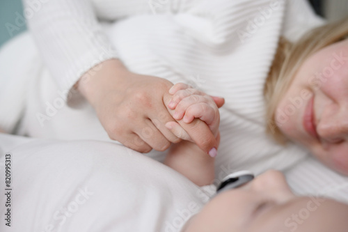 Baby holds mom hand. Close up of loving mom touching little baby hand, sleeping baby on bed with pacifier enjoying tender moment. Concepts of motherhood and tenderness, childbirth, motherhood concept.