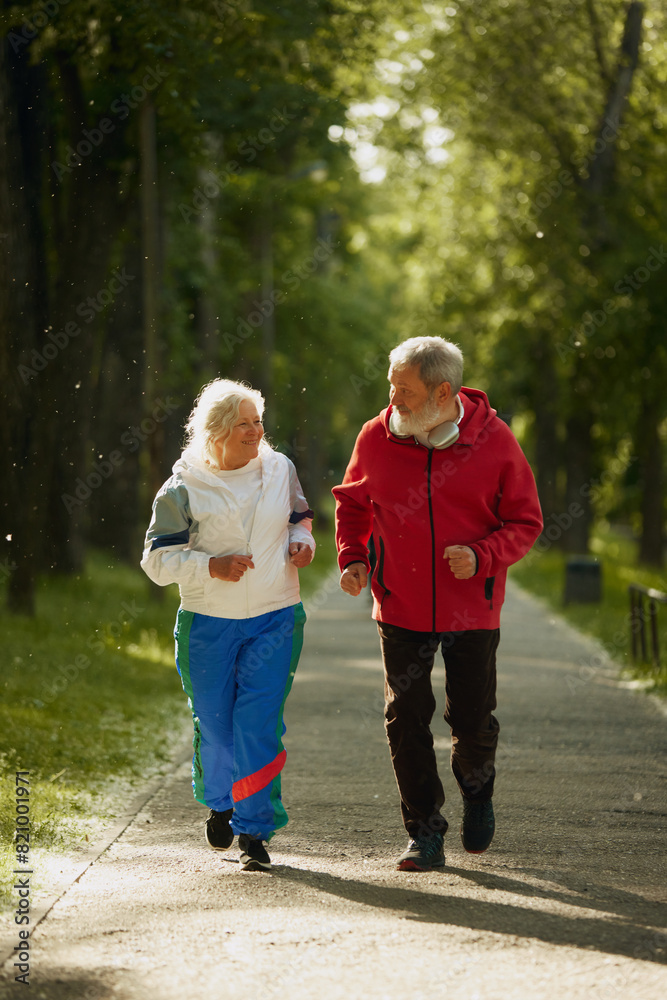 Fototapeta premium Elderly and active man and woman, positive couple in sportswear energetically jogging in early morning park, training. Concept of sport, aging, active and healthy lifestyle, health care