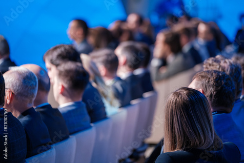 Group of professionals listening attentively during a business conference in a contemporary setting. The scene captures focus and engagement among the attendees.