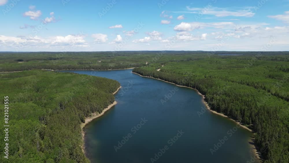 Aerial view from a drone moving forward over a dark blue colored lake that is surrounded by a vast evergreen forest. The sky is bright blue with white summer clouds.
Aerial view from a drone moving forward over a dark blue colored lake that is surrounded by a vast evergreen forest. The sky is bright blue with white summer clouds.