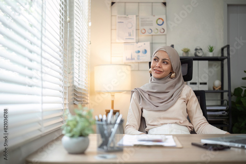 Smiling Muslim woman sitting at office desk. Professional workspace, casual attire