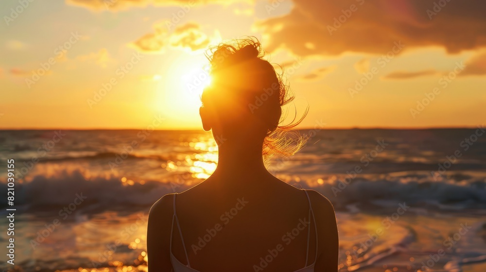 Silhouette of a woman looking at the beach and the ocean at sunset from behind.