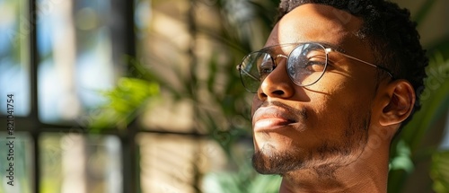 Young black man, in contemplative mood, enhances his flawless, youthful skin with facial serum by the window in sunlight photo