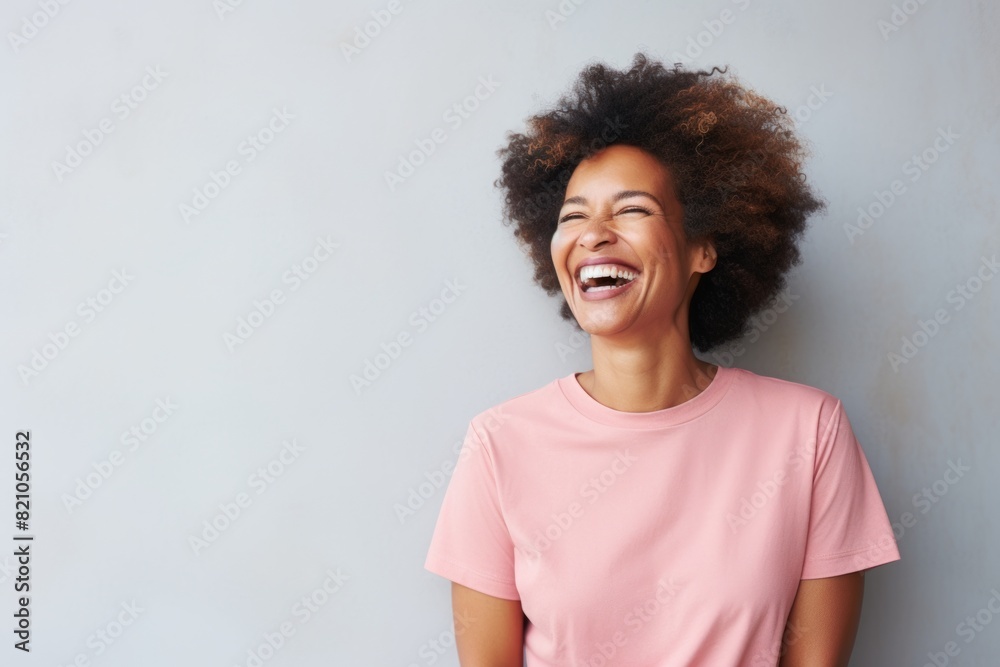 Portrait of a joyful afro-american woman in her 50s laughing while standing against minimalist or empty room background