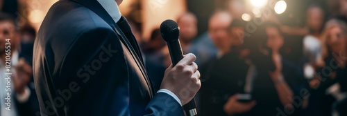 Close-up of a speaker holding a microphone, addressing an unseen, blurred audience photo