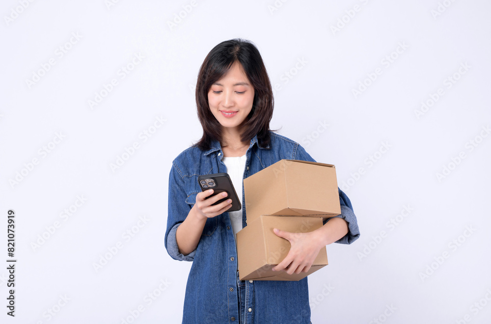 asian woman wearing denim jean holding parcel box while using mobile phone isolated on white studio background, Delivery courier and shipping service concept. asian woman wearing denim jean holding parcel box while using mobile phone isolated on white studio background, Delivery courier and shipping service concept.