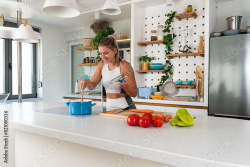 Young sporty woman preparing a health meal during menstrual period. Female cooking vegetables in domestic kitchen while she have menstruation. Health eating with organic food, lunch after home workout