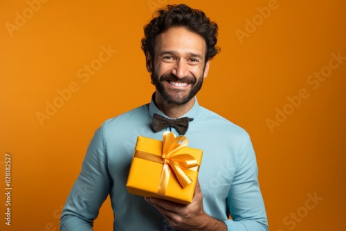 Portrait of a happy man in his 30s holding a gift in front of solid color backdrop © Markus Schröder