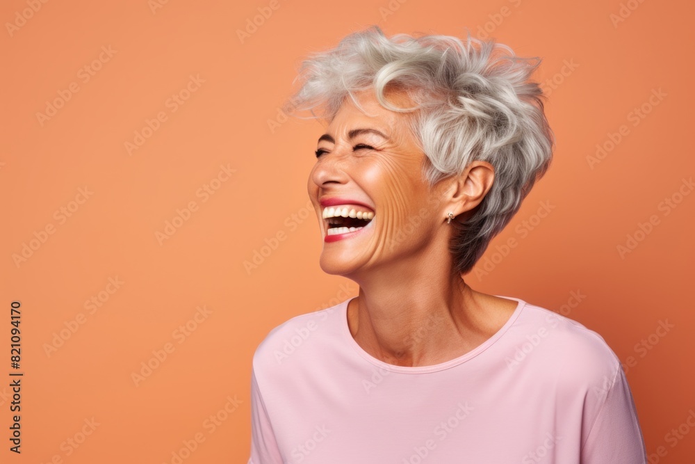 Portrait of a smiling woman in her 60s laughing isolated in solid color backdrop
