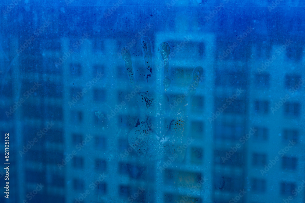 Fototapeta premium A hand is visible through a window of a building. The hand is partially covered by the window, but it is clear enough to see the outline of the hand. The building is tall and has many windows