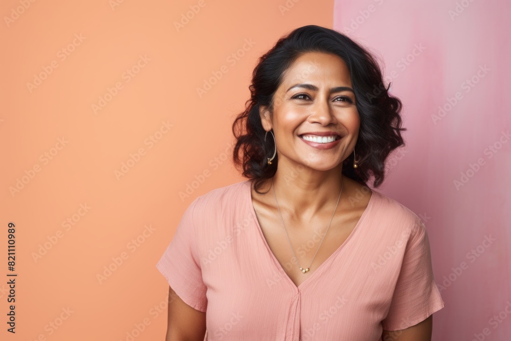 Portrait of a satisfied indian woman in her 40s smiling at the camera in front of solid pastel color wall Portrait of a satisfied indian woman in her 40s smiling at the camera in front of solid pastel color wall