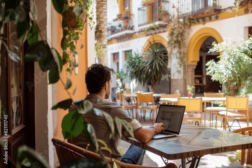 digital nomad expat working on laptop at cafe terrace or coworking in a narrow street of a town in Spain in summer