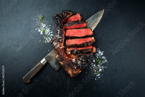 Barbecue dry aged chianina rib of beef steak served with crystal salt and thyme as top view on a black design board with a large butcher knife