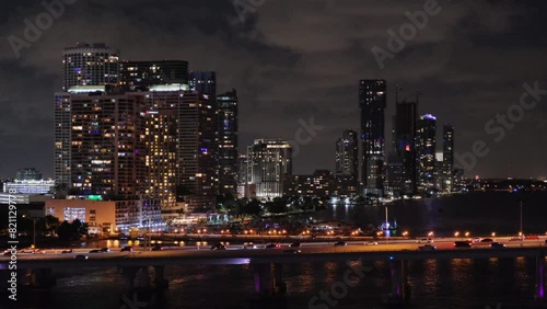Wallpaper Mural View of night downtown Miami, Florida, silhouettes of skyscrapers against dark cloudy sky, reflection of light in water surface, cars driving along bridge lit by street lamps, camera tracking along . Torontodigital.ca