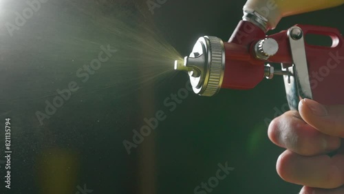 Close-Up of Red Spray Gun in Action with Yellow Paint in Workshop