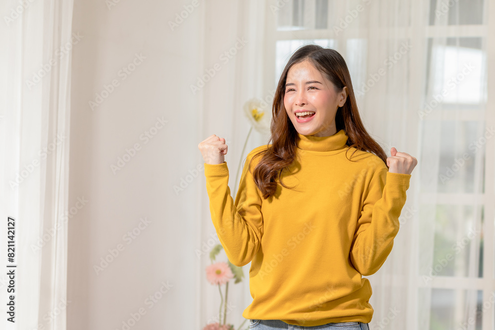 Happy woman in yellow sweater celebrating success indoors, showing joy and excitement with raised fists. Bright interior background. Happy woman in yellow sweater celebrating success indoors, showing joy and excitement with raised fists. Bright interior background.