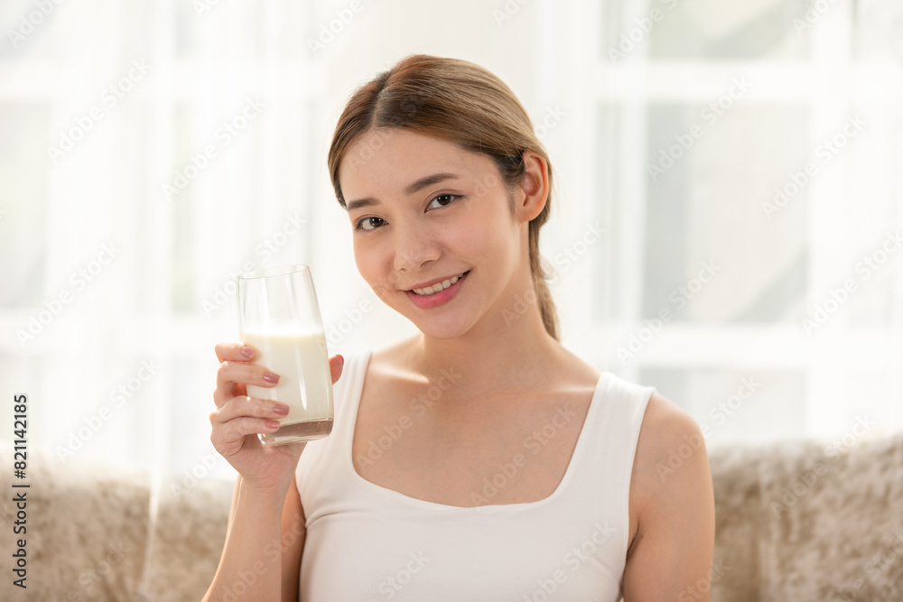 Smiling woman enjoying a glass of milk at home, promoting a healthy lifestyle and balanced diet in a bright and serene setting. Smiling woman enjoying a glass of milk at home, promoting a healthy lifestyle and balanced diet in a bright and serene setting.