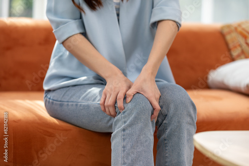 Person experiencing knee pain while sitting on a couch. Concept of joint discomfort, injury, and rehabilitation.