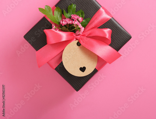 Black craft gift box with empty round tag, hawthorn flowers on pink background. Place for your text