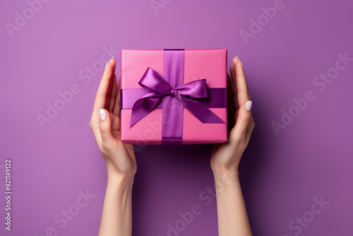 romantic purple or magenta background with woman hands holding a wrapped gift box seen from above for a birthday