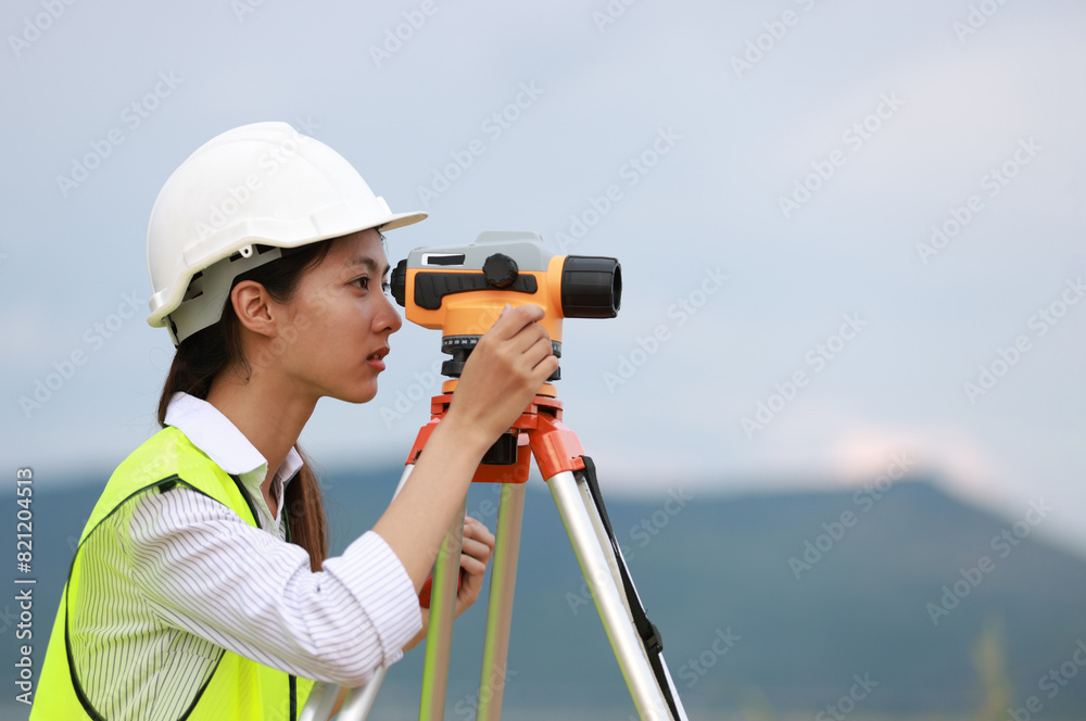 Obraz premium Portrait beautiful Asian construction engineer with a green safety vest hard hat and level survey camera.Engineer peering through a theodolite