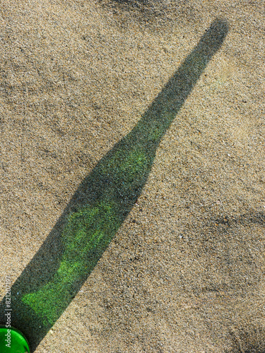 Shadow from empty green bottle under the sunlight on sand.