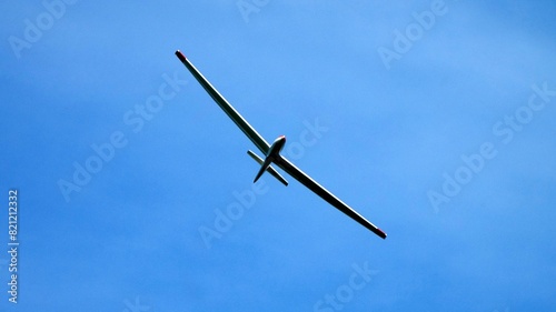 Glider concept: aerial view of a glider flying alone isolated in the blue sky