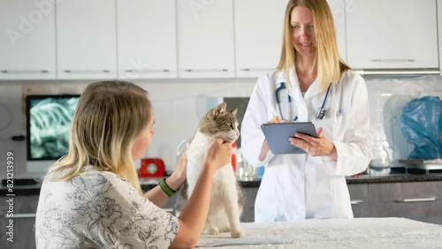 Pet owner strokes his cat at a veterinarian's appointment with a tablet recording anamnesis of an illness in an animal hospital against the background of an x-ray on screen.