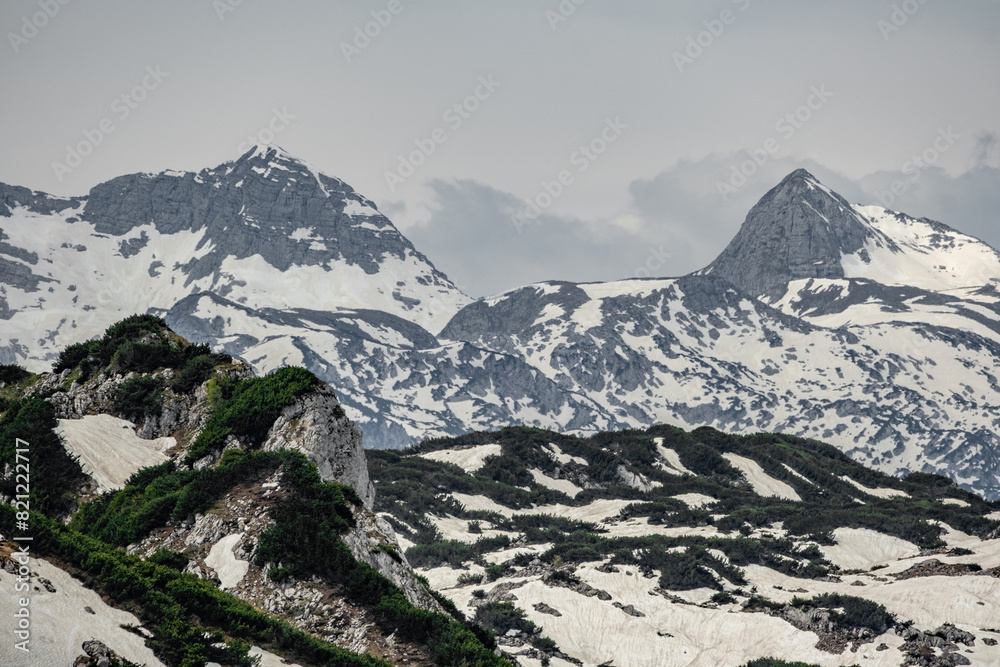 Fototapeta premium The view depicts a mountain towering over a valley, with lush greenery contrasting the rugged terrain.