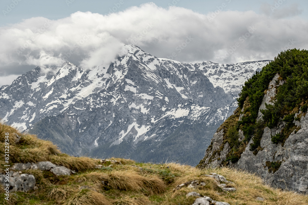The view depicts a mountain towering over a valley, with lush greenery contrasting the rugged terrain.