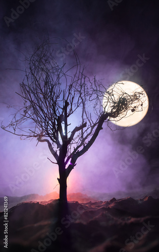 Silhouette of scary Halloween tree with horror face on dark foggy toned background with moon on back side. Scary horror tree with zombie and monster demon faces.
