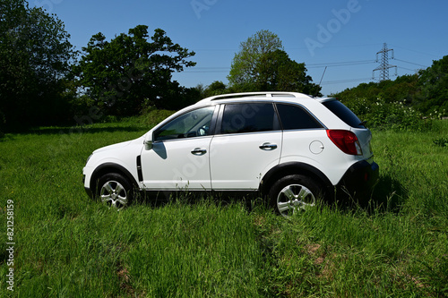 White SUV parked in a long grass field in the English countryside in summer time. 