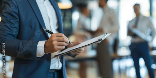 A business man in a suit taking notes on a clipboard in a corporate environment