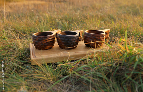 Three wooden Finnish mugs on a wooden board on dry grass in nature