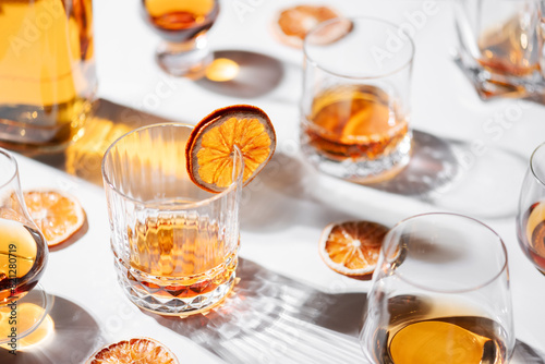 Different shape glasses with whiskey on white table. Dried oranges decoration. Alcohol concept