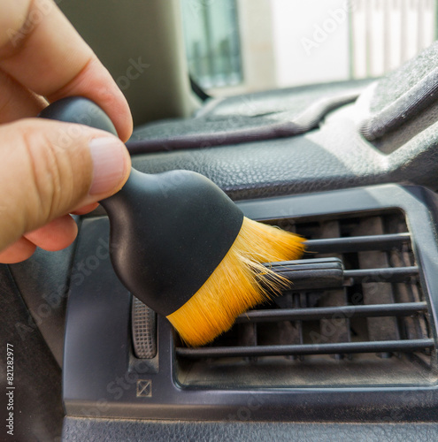 A person uses a special cleaning brush to clean and remove dust from the air conditioning outlet of the car.