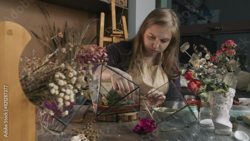 Decorative stones add a touch of elegance to the floral arrangement, which is placed in a glass, polygonal vase. The vase holds a variety of small succulents, and the arrangement is complemented by a photo