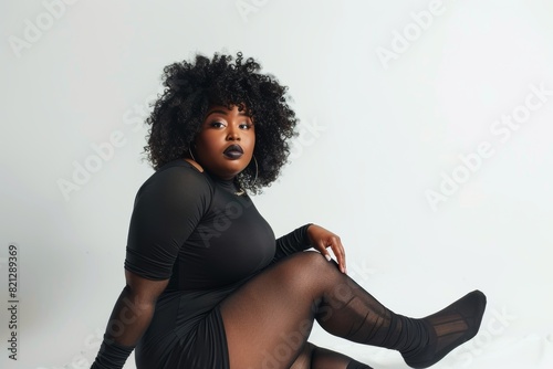 Confident plus size model in black hosiery and dress against white background photo