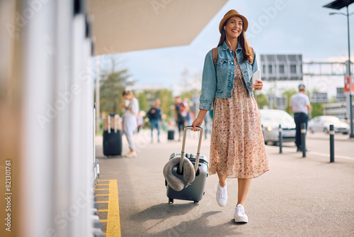Happy traveler pulling her suitcase while walking at station.