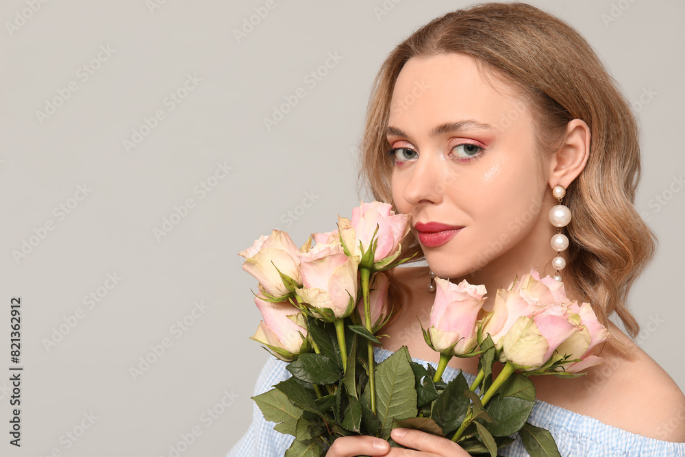 Pretty young woman with bouquet of beautiful roses on grey background