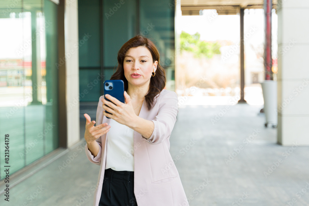 Busy businesswoman using her smartphone for a video call while commuting in the city in a professional yet casual attire Busy businesswoman using her smartphone for a video call while commuting in the city in a professional yet casual attire