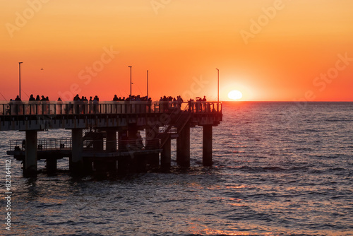 Wallpaper Mural Many people watch the sunset from the pier over the sea. The orange sun was half hidden behind the horizon. Background. Torontodigital.ca