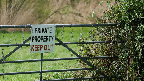 A sign for private property keep out on a metal gate with coiled barbed wire to farmland field photo