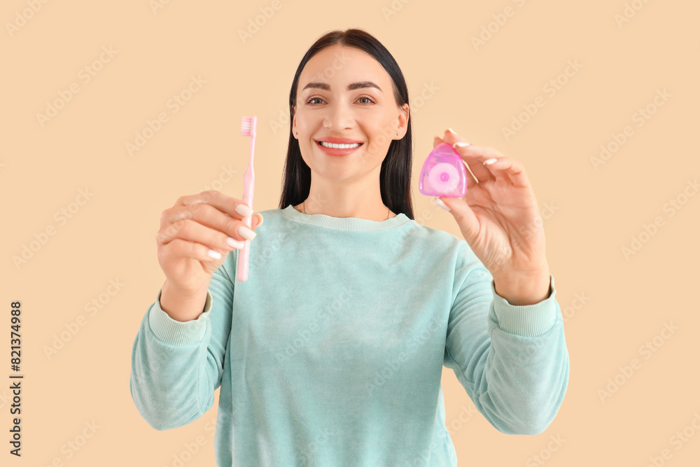 Beautiful young happy woman with dental floss and toothbrush on beige background